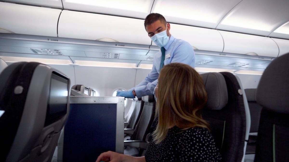 Aer Lingus cabin crew wearing a mask and gloves interacting with a passenger