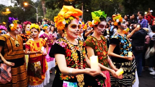 Women in colourful traditional dresses and face paint participating in a cultural parade.