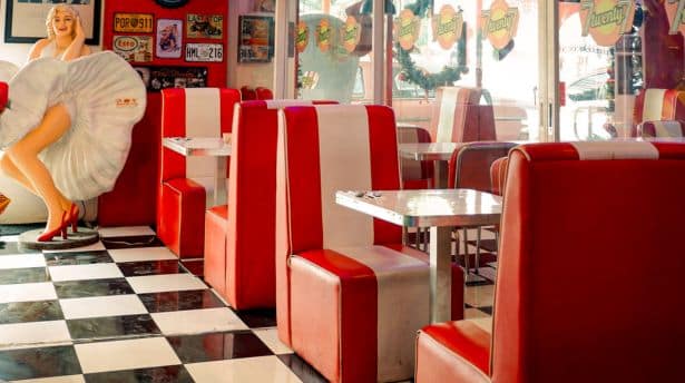 Retro-style diner with red and white booth seating, checkered floor, vintage décor, and a Marilyn Monroe statue.
