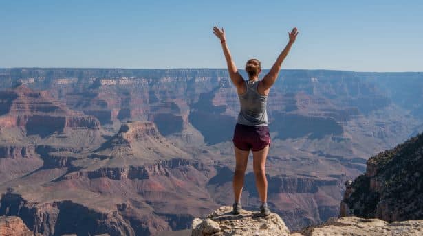 Woman standing with arms raised at the edge of the Grand Canyon, admiring the vast red rock landscape.