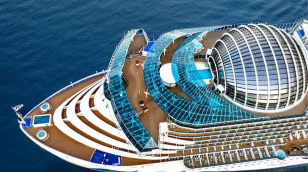 Top-down view of a cruise ship’s multi-level, curved glass structures and decks, highlighting a striking atrium and observation areas.