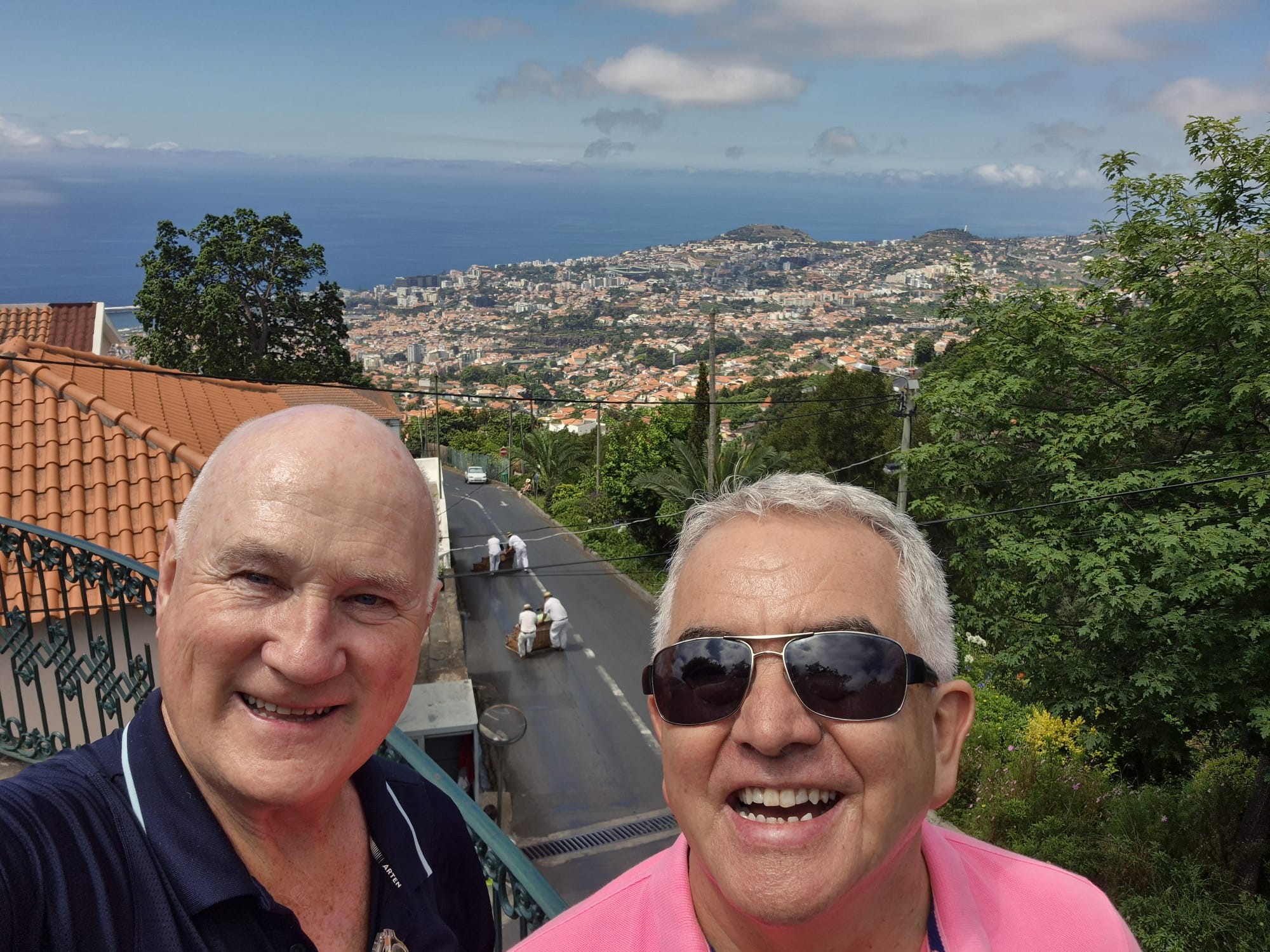 A selfie on a hill overlooking a coastal city in Madeira, with terracotta rooftops, lush greenery, and the Atlantic Ocean in the background.