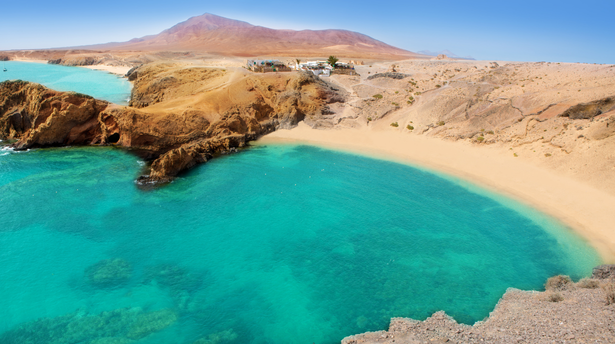 Crystal-clear turquoise water and a sheltered sandy cove surrounded by volcanic rock cliffs in Lanzarote