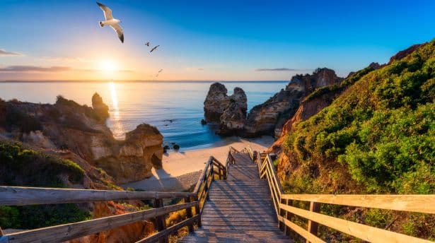 Wooden steps leading down to a golden beach in the Algarve with dramatic cliffs and Atlantic Ocean at sunset