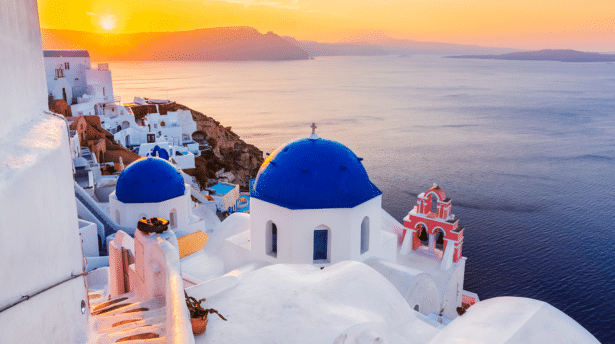 Iconic blue domes and white buildings in Santorini overlooking the Aegean Sea at sunset