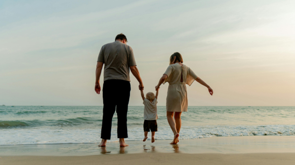 Family holiday moment on the beach with child held between parents near the shoreline