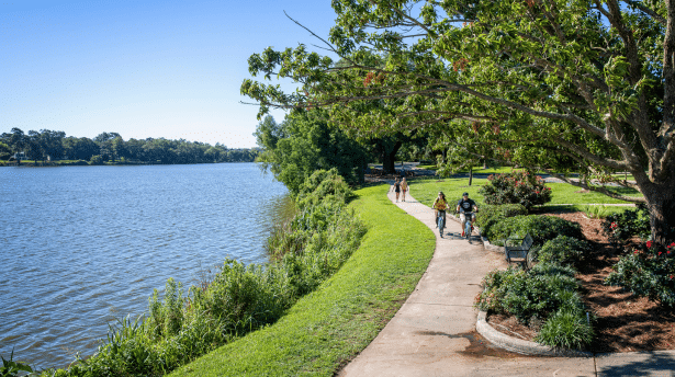 Scenic riverside walkway in Baton Rouge with people cycling and walking along the Mississippi River under green trees