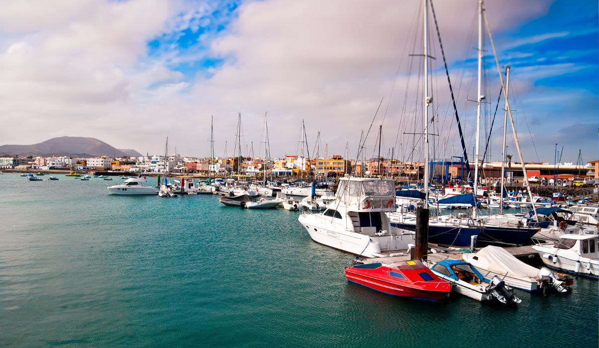 Busy scene at Corralejo Marina in Fuerteventura with colourful boats and yachts docked under cloudy skies.