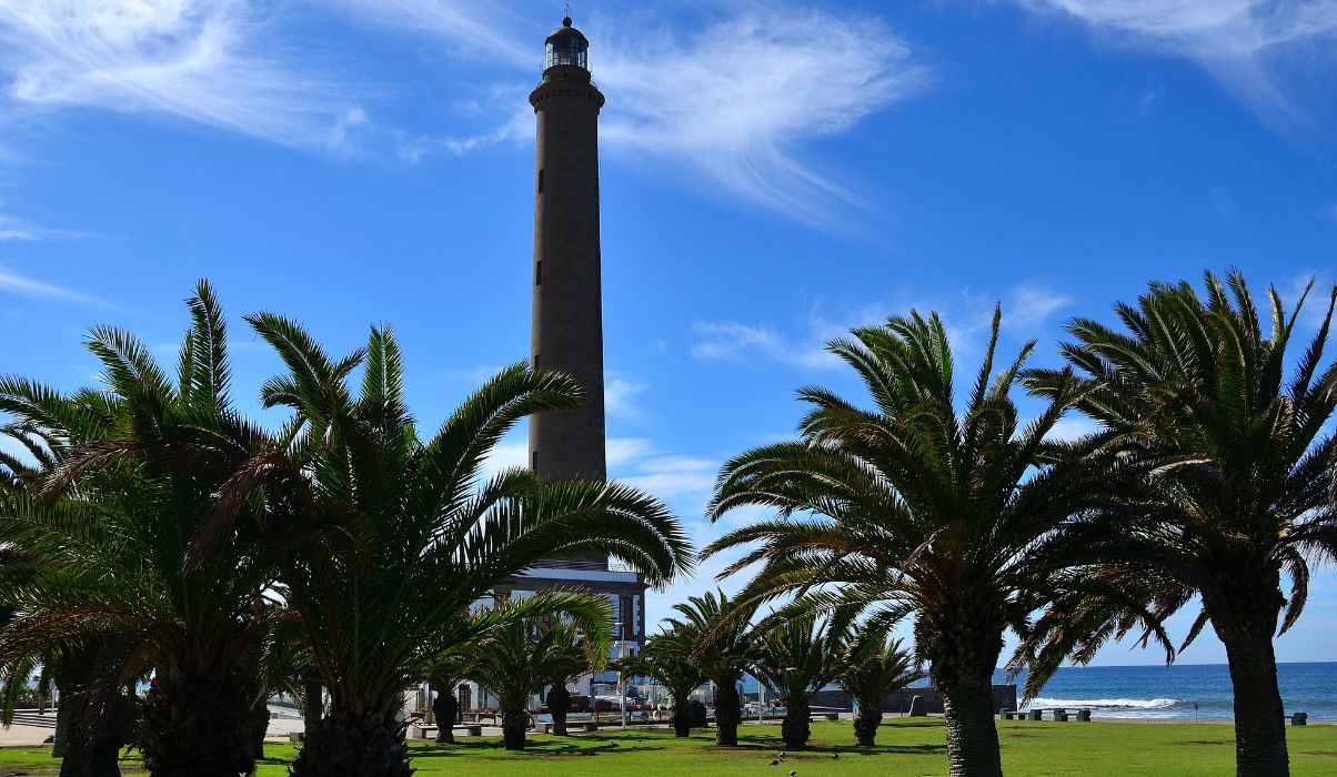 Iconic Maspalomas Lighthouse surrounded by lush palm trees against a clear blue sky in Gran Canaria.