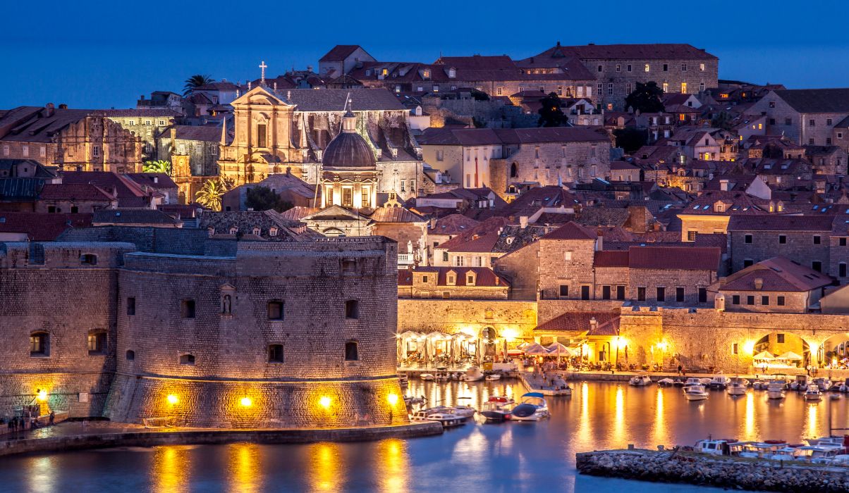 Night view of Dubrovnik with illuminated city walls and historic buildings reflecting in the harbour.