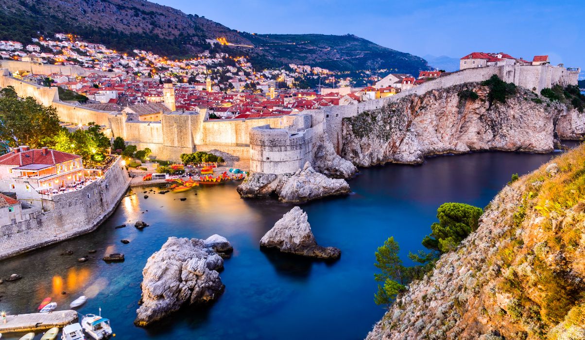 Dramatic evening view of Dubrovnik's old town with city lights reflecting off the calm Adriatic Sea.