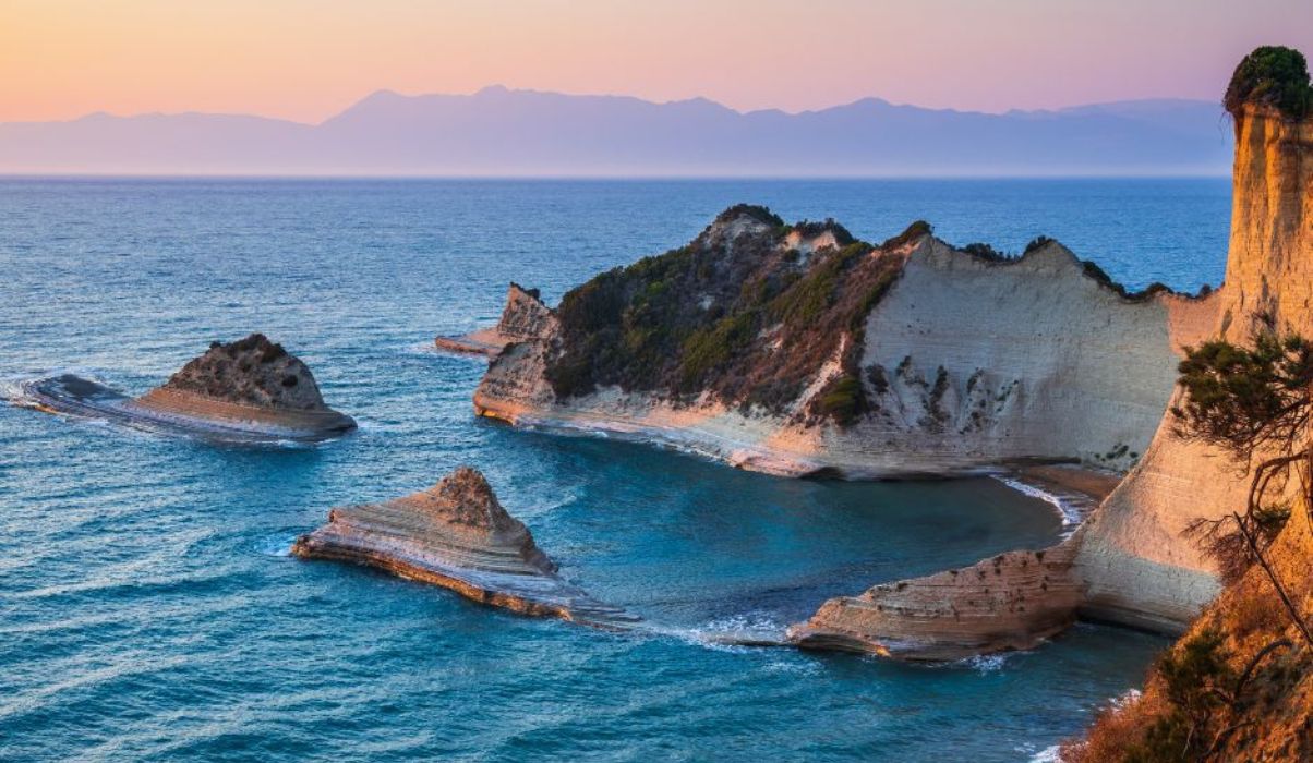 Breathtaking view of sunset colours illuminating the cliffs and waters at a secluded beach in Corfu.