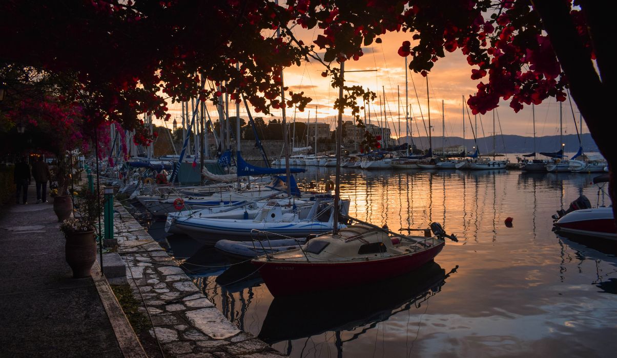 Dramatic sunset in Corfu with silhouettes of people walking along the beach and reflective waters.