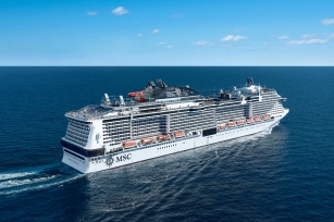 side view of the MSC Bellissima featuring the branding of MSC on the side of the cruise ship cruising through the deep blue sea and clear blue skies